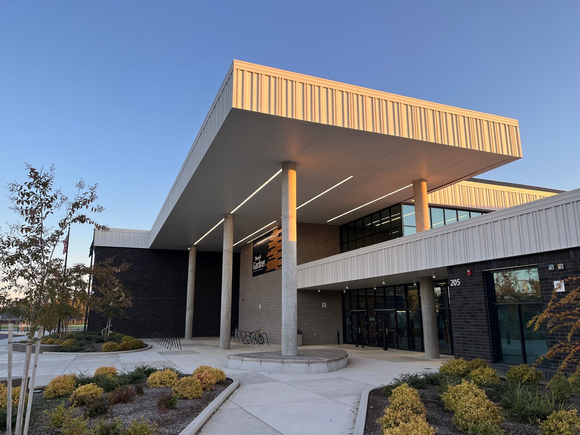 Modern concrete building with angular roof, glass walls, and desert landscaping at sunset