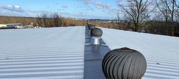 Metal roof with two rooftop vents under a blue sky, with trees in the background