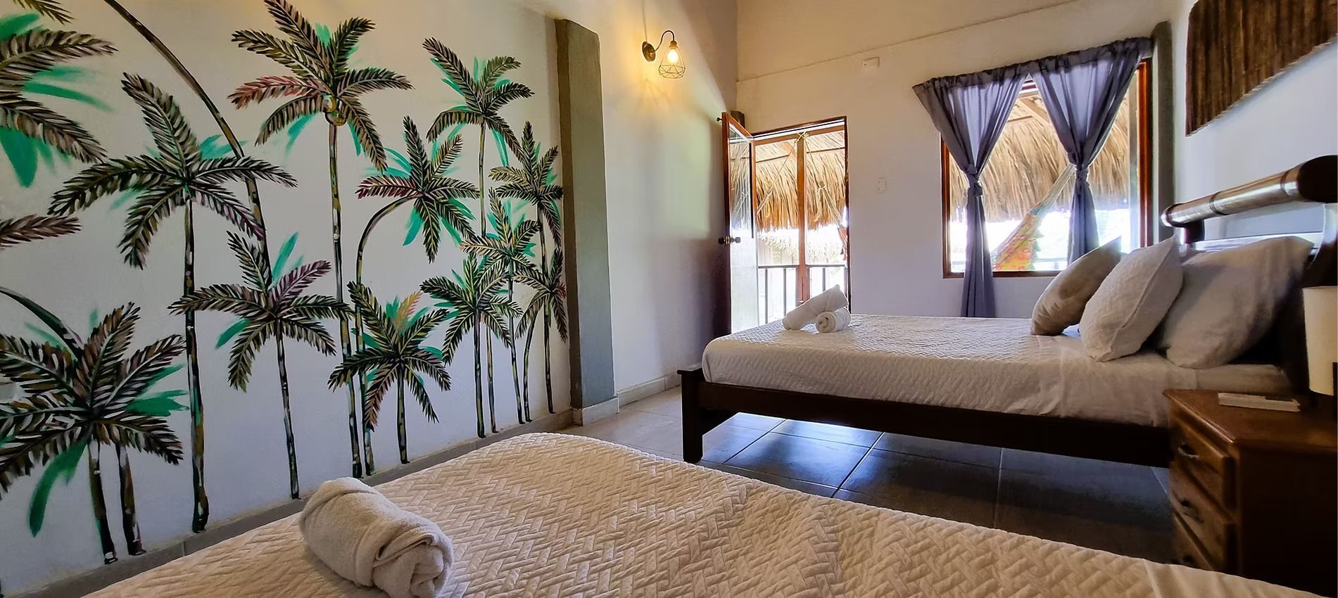 A bedroom with two beds and a painting of palm trees on the wall.