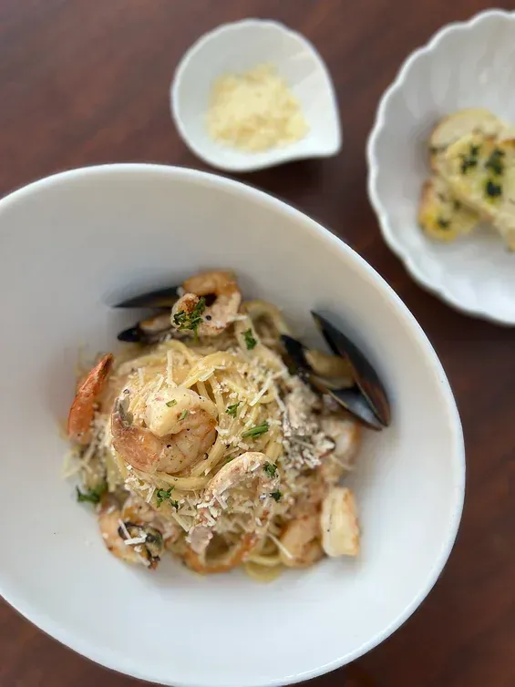 A bowl of pasta with shrimp and mussels next to a bowl of garlic bread.