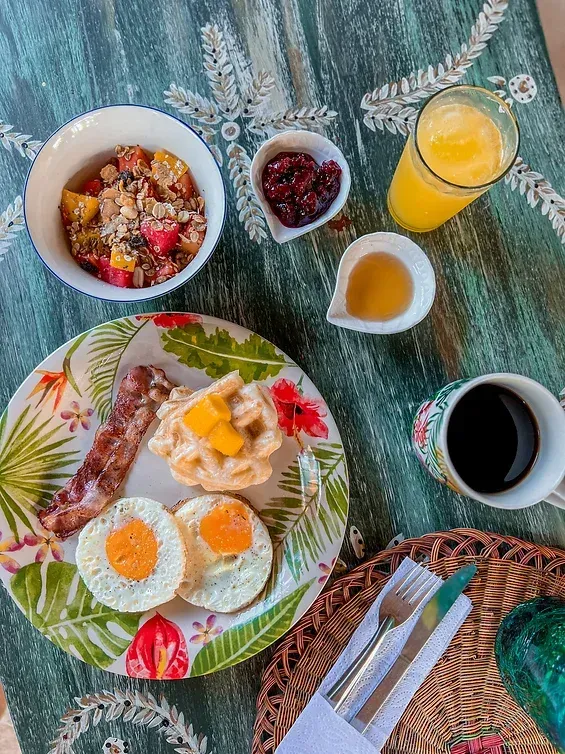A plate of food with eggs , bacon , waffles , oatmeal , and juice on a table.