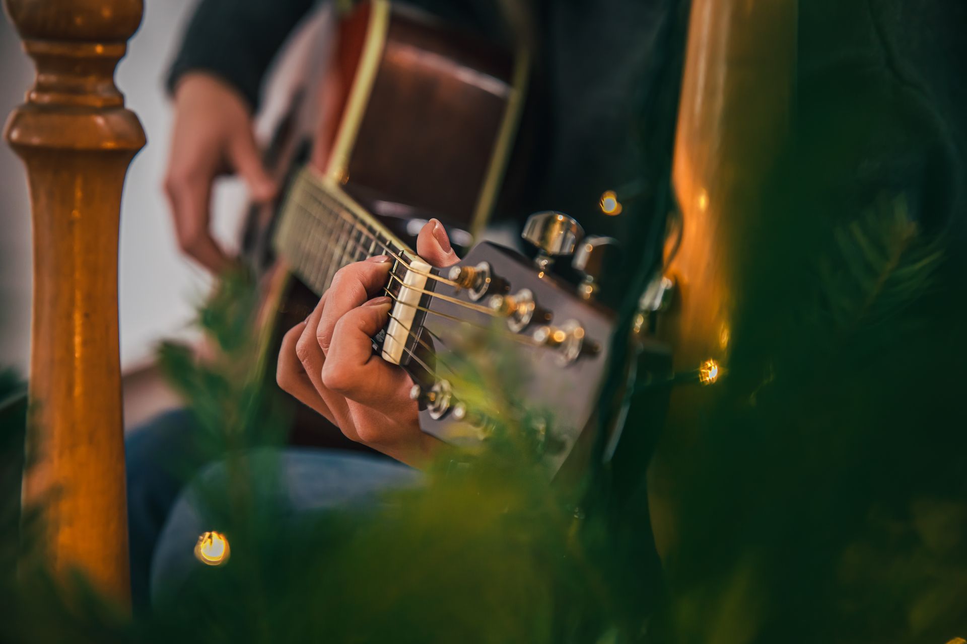 A man is playing an acoustic guitar in front of a christmas tree.