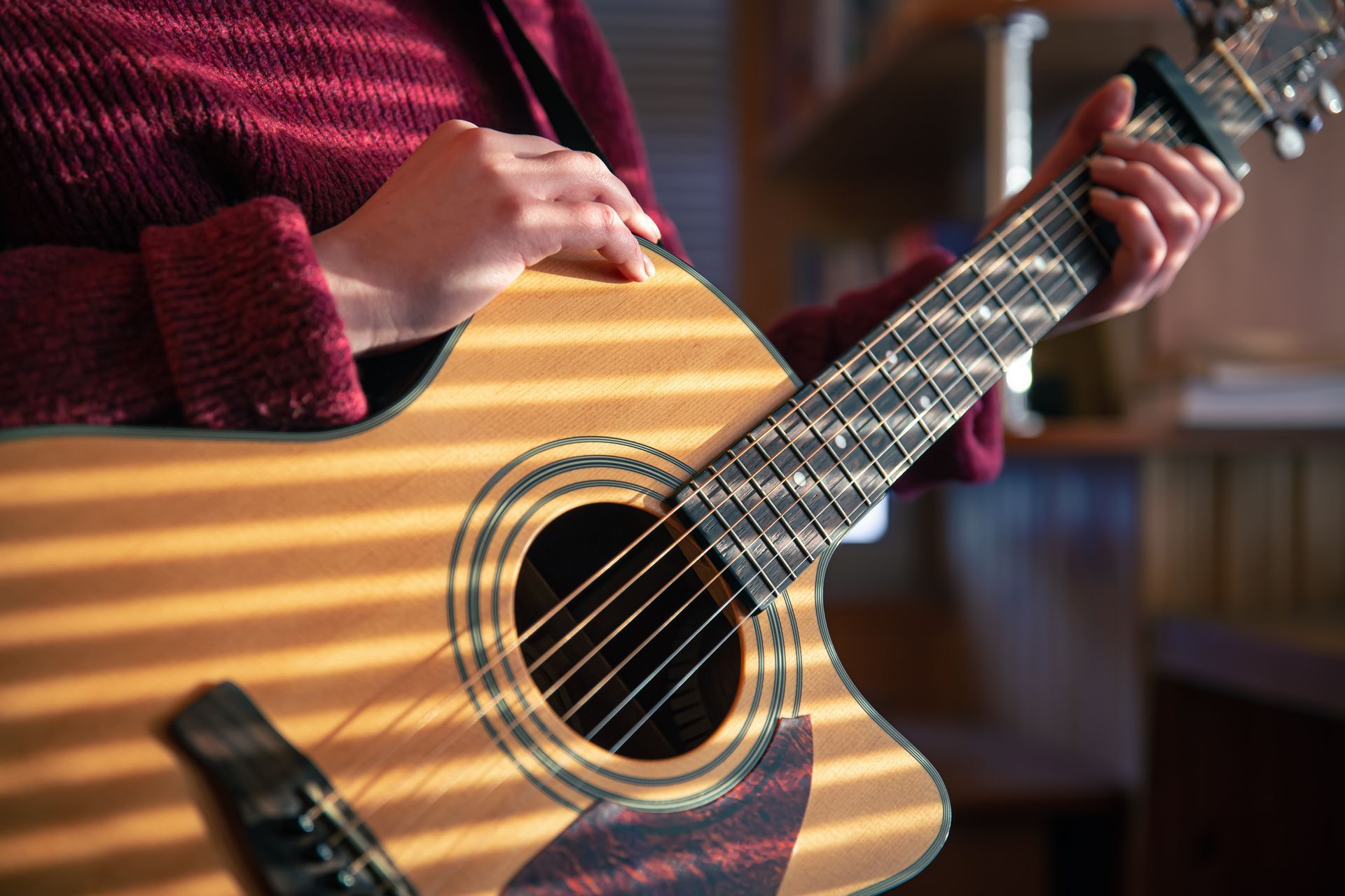 A woman in a red sweater is playing an acoustic guitar.
