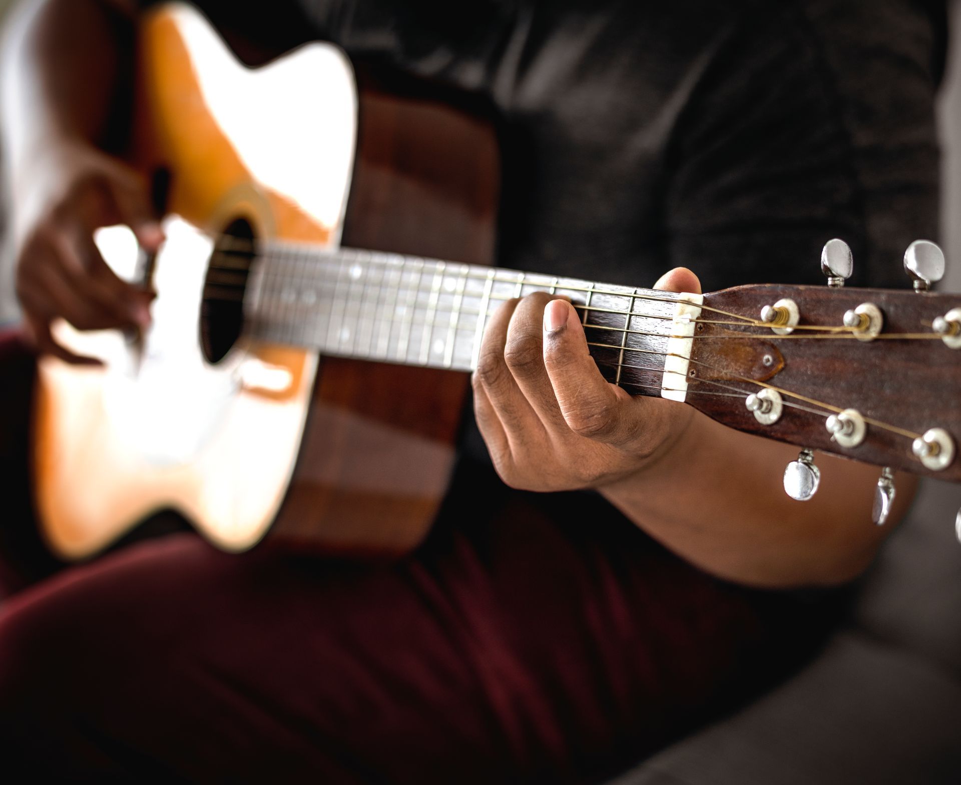 A man is playing an acoustic guitar while sitting on a couch.