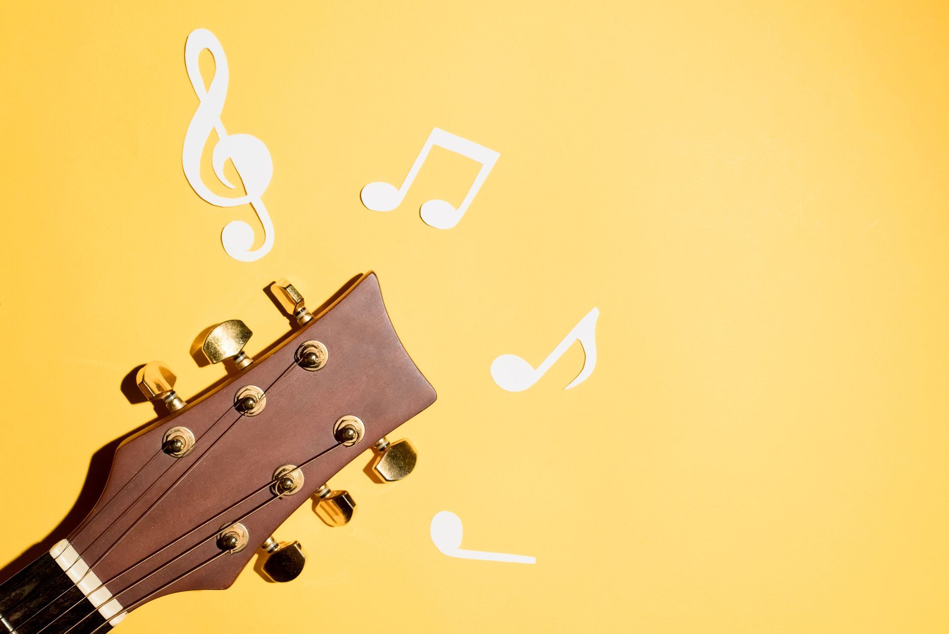 A guitar headstock with music notes coming out of it on a yellow background.