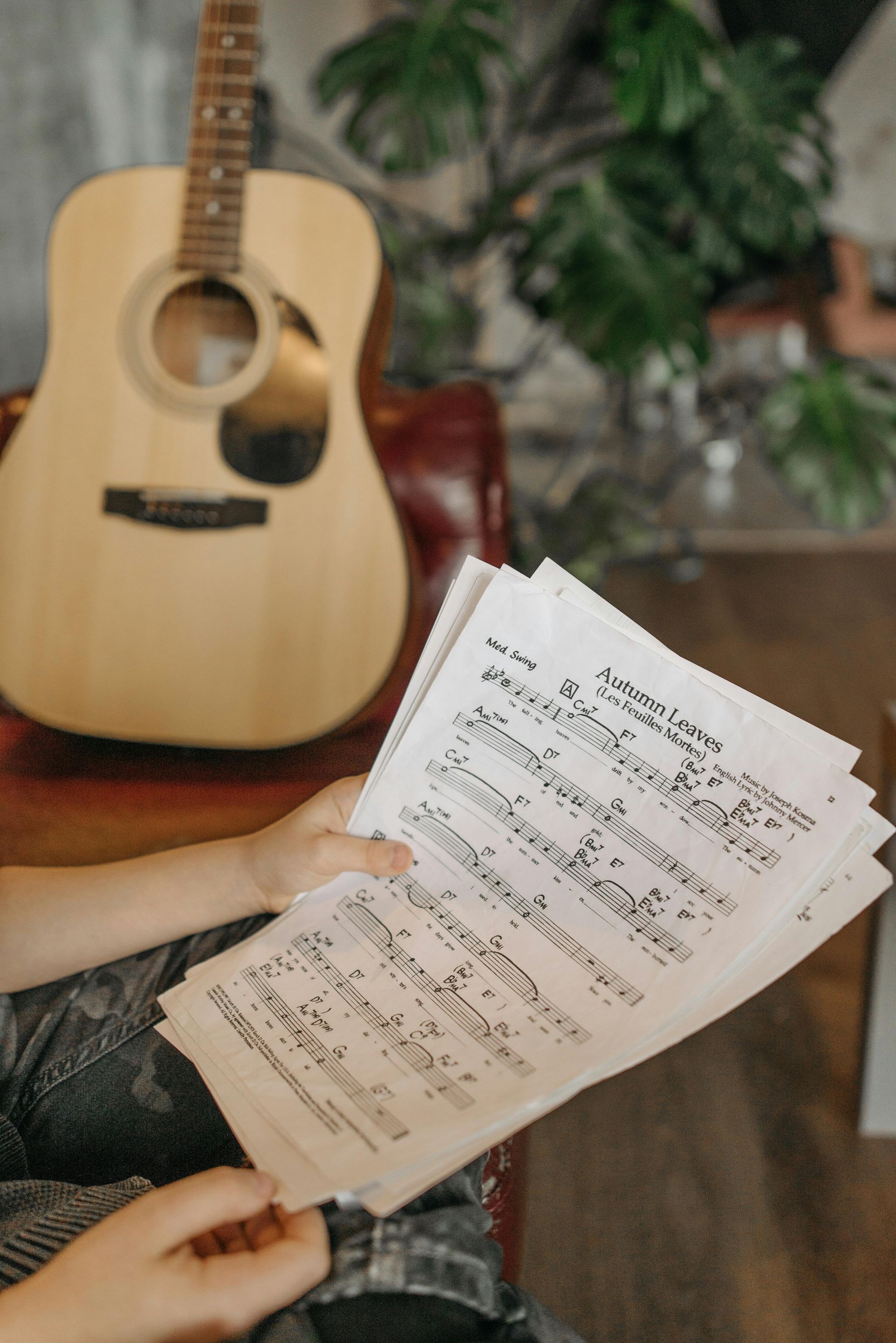 A person is holding a stack of sheet music in front of a guitar.