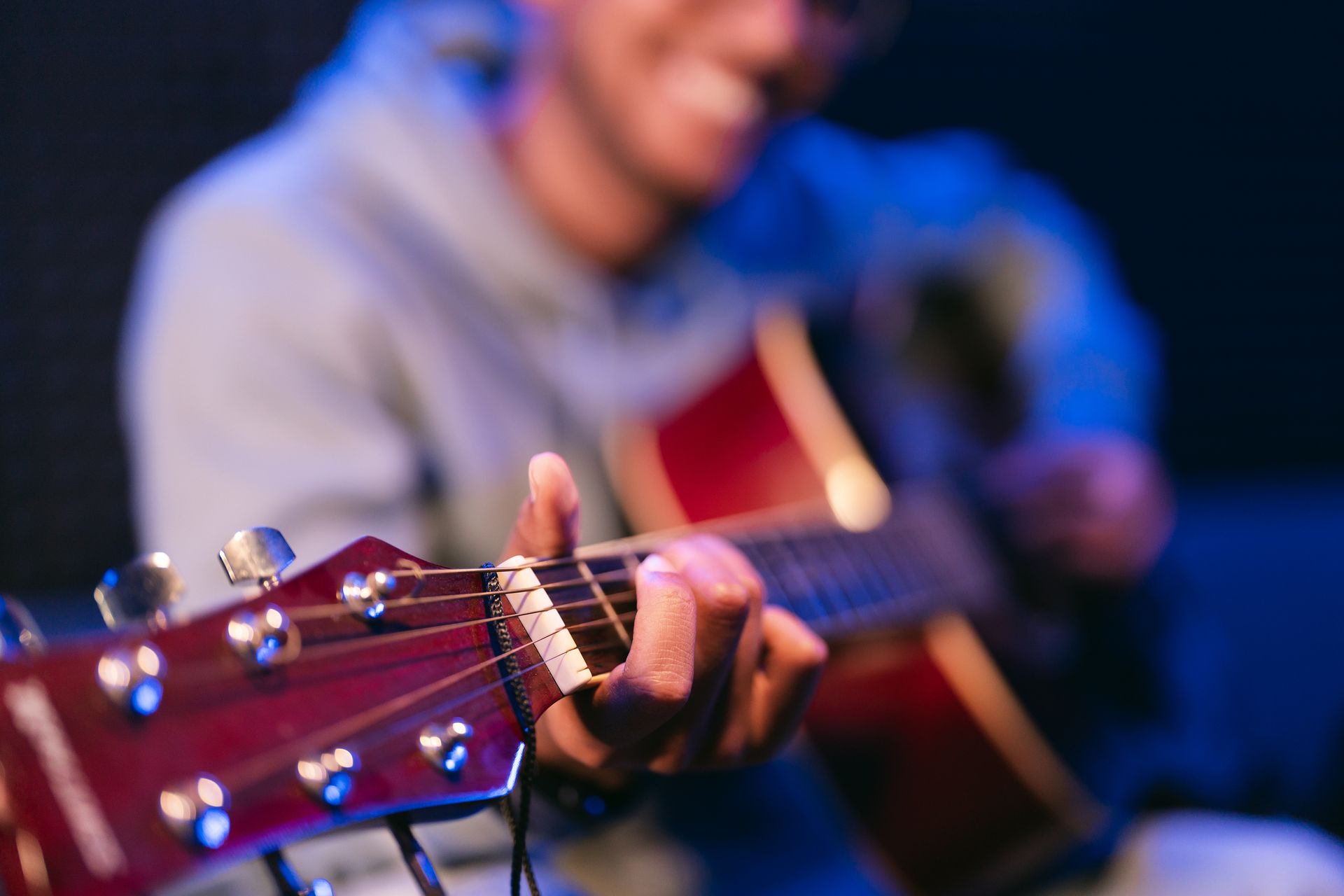 A man is playing an acoustic guitar in a dark room.