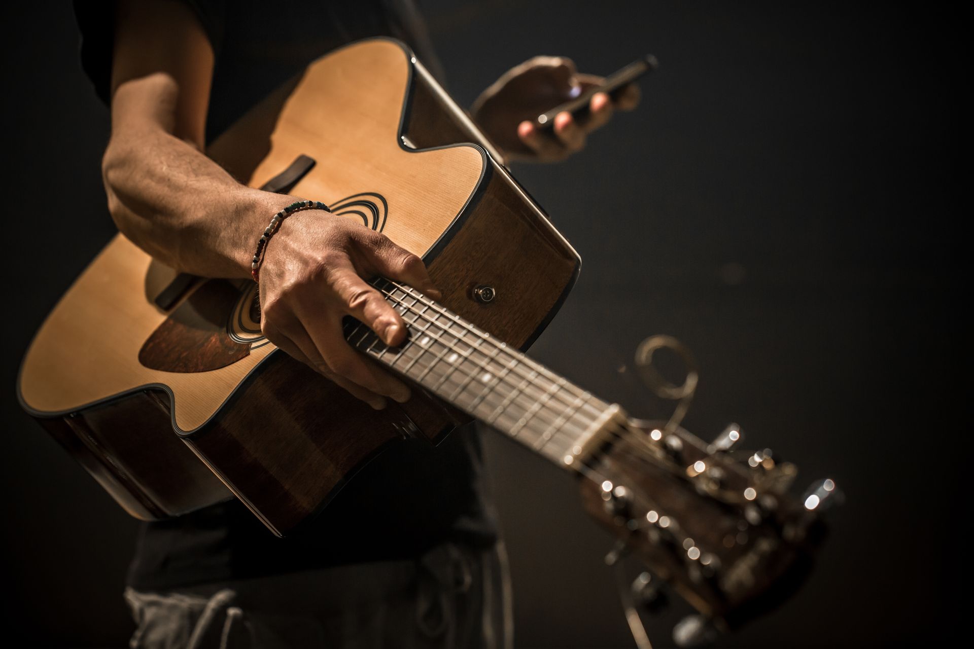 A man is playing an acoustic guitar while holding a cell phone.