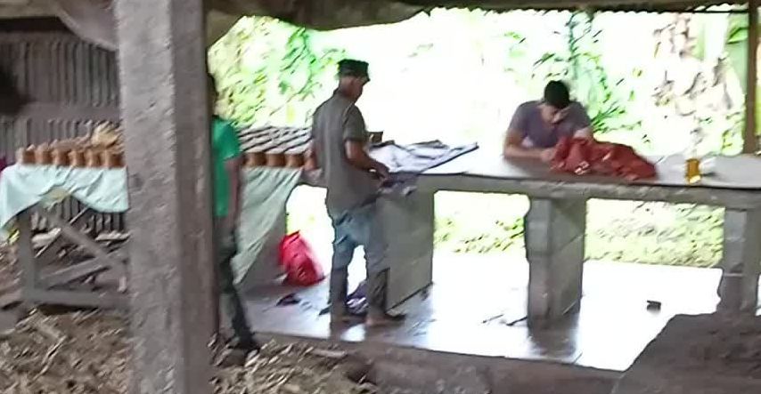 A group of men are standing around a table in a shed.