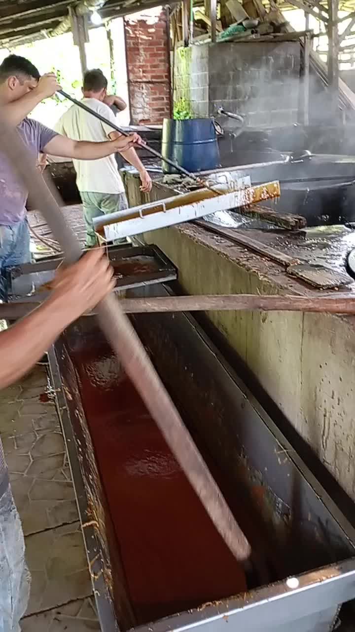 A man is stirring a large container of liquid with a wooden stick.
