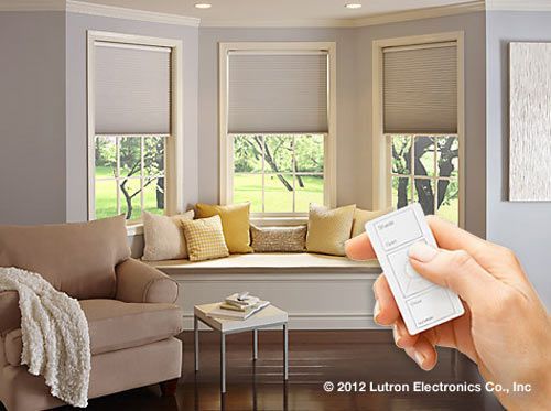 A person holding a remote controls motorized window shades in a bright living room.
