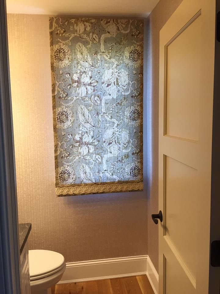 Small bathroom with floral window shade, toilet, and open door. Pinkish-tan walls, cream door, light wooden floor.