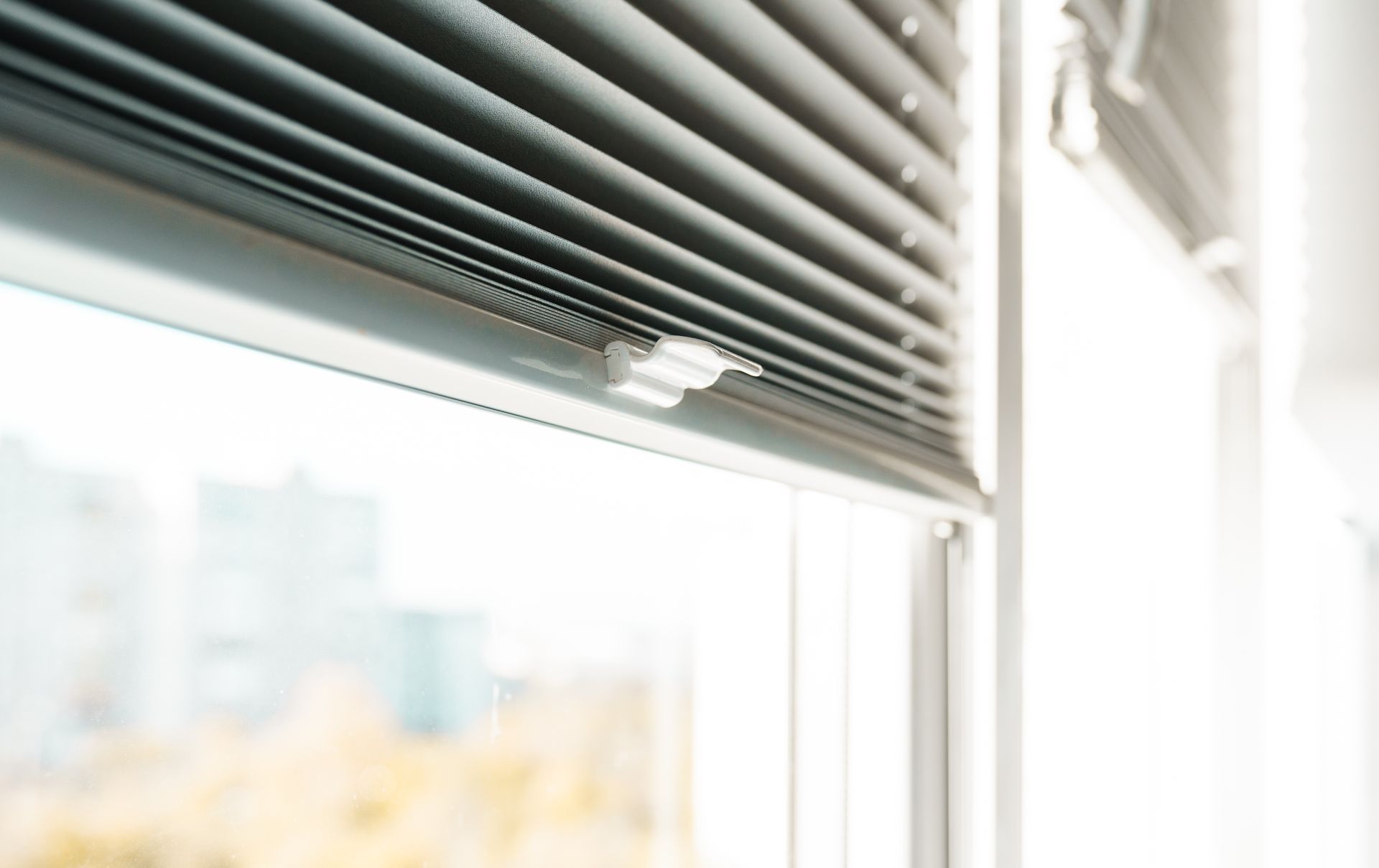 Close-up of partially open gray blinds in a window with a blurred outdoor view.