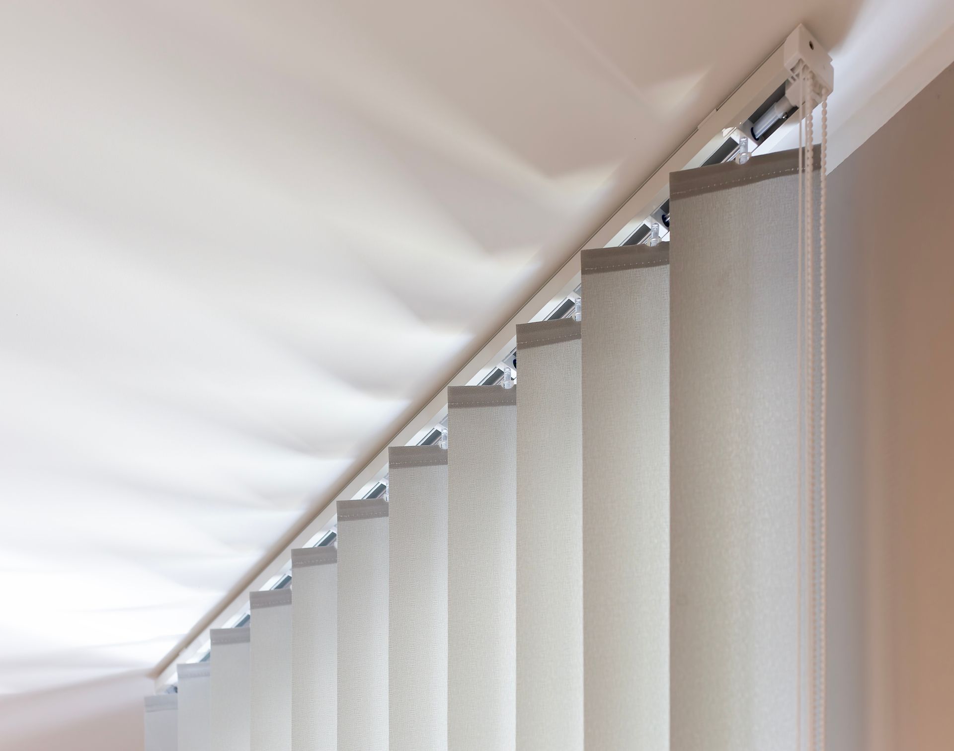 White vertical blinds partially covering a window, viewed from a low angle.