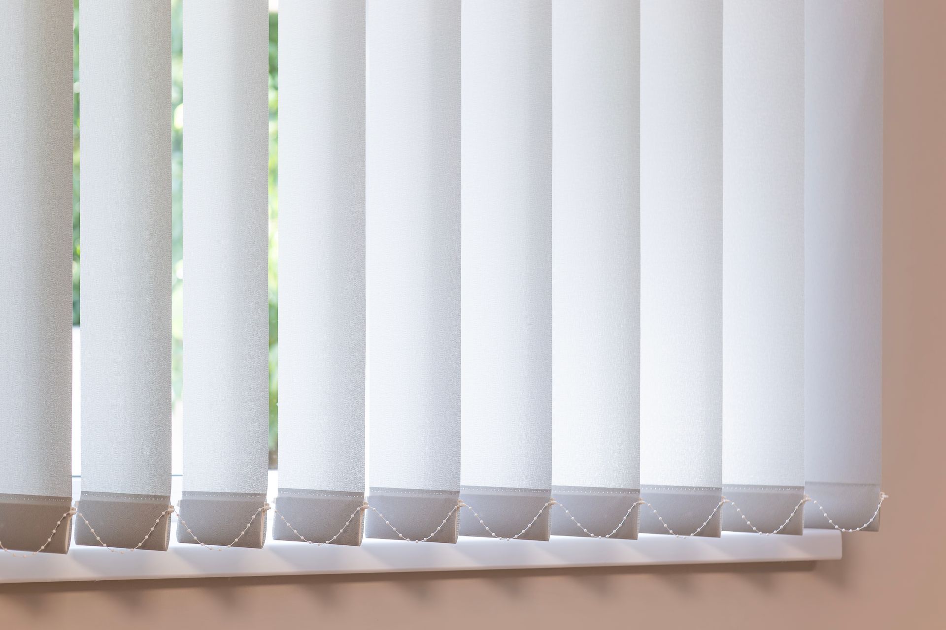 White vertical blinds over a windowsill, partially open, with natural light visible.