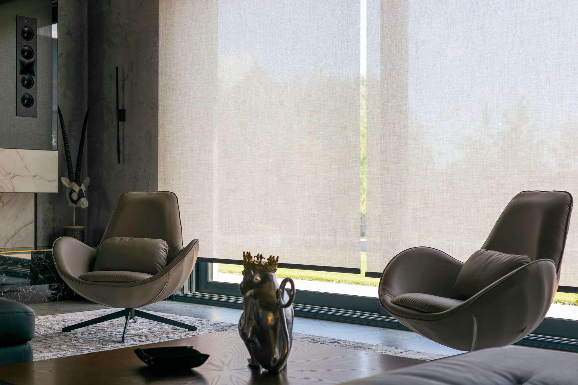 Two modern armchairs in a living room, near a large window with sheer blinds.