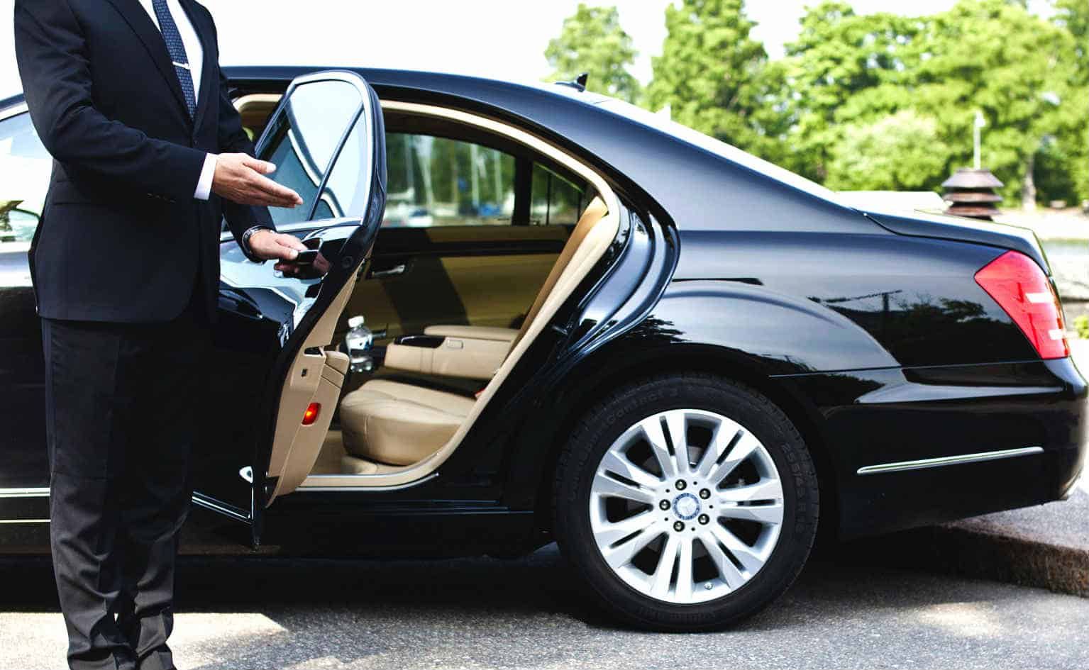 A man in a suit and tie is getting out of a black car.