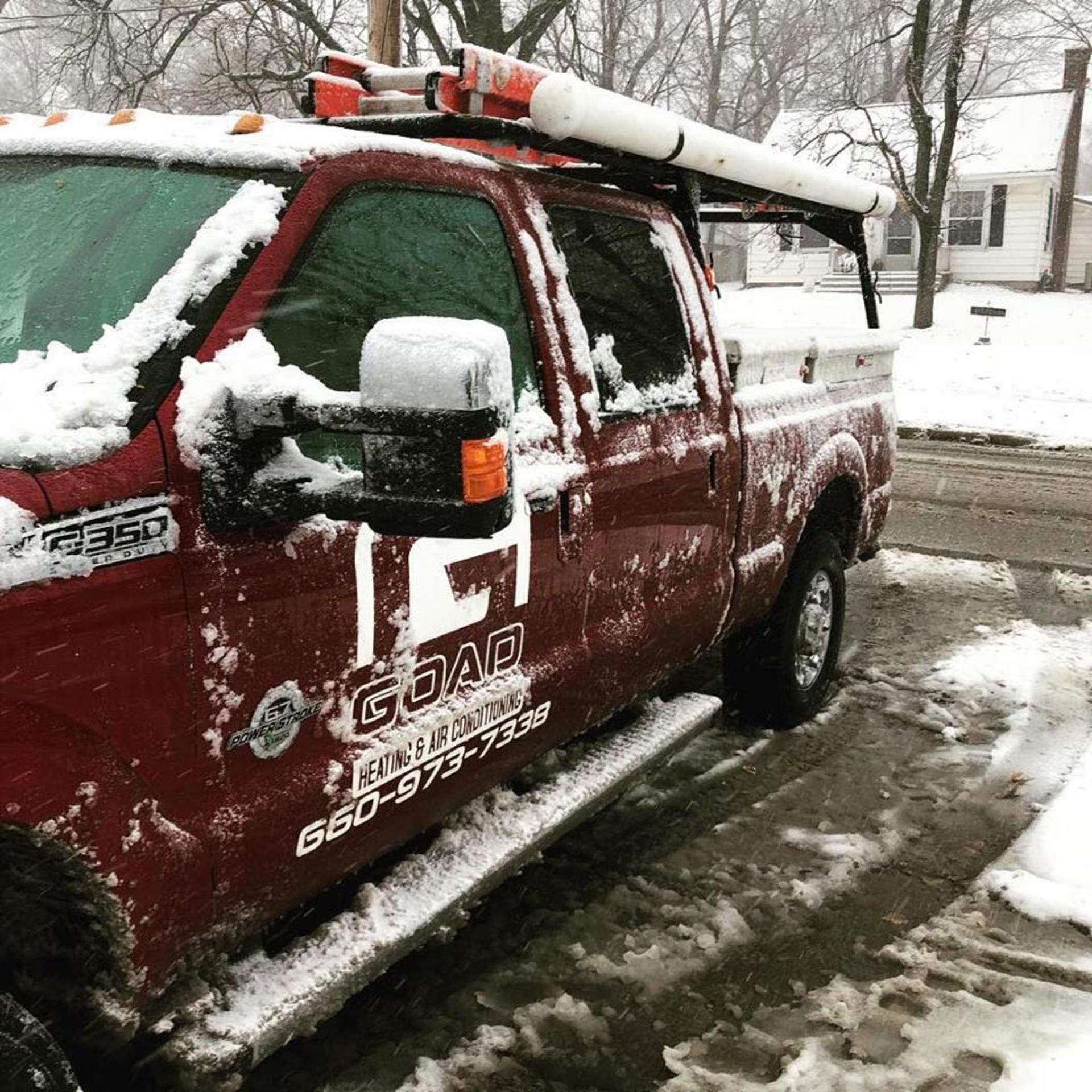 A red truck with a ladder on top of it is parked in the snow