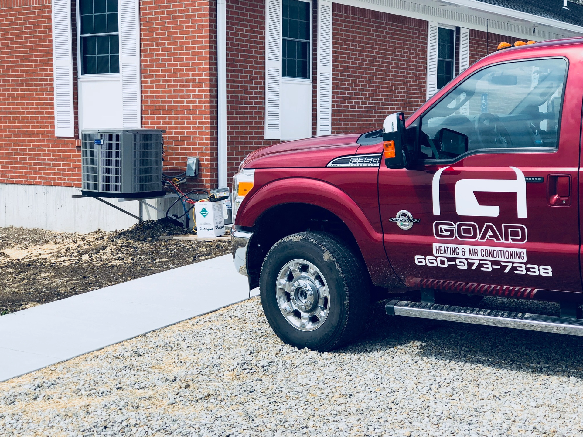 A red goad truck is parked in front of a brick building.