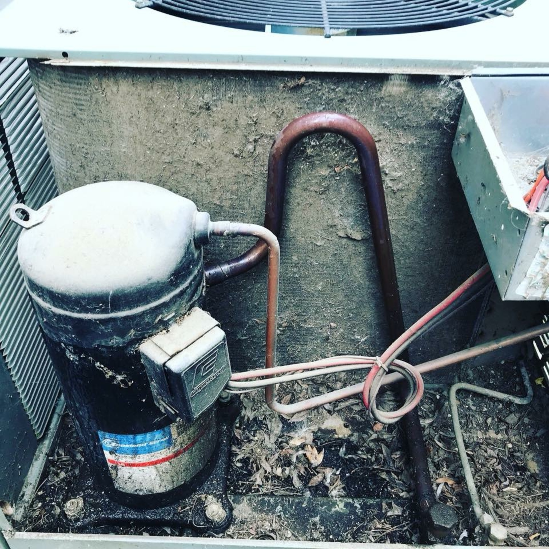 A dirty air conditioner with a compressor and copper pipes.