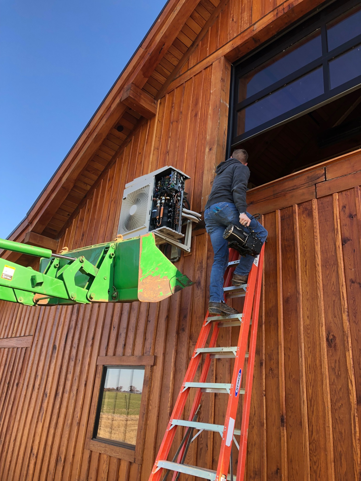 A man is standing on a ladder in front of a wooden building.