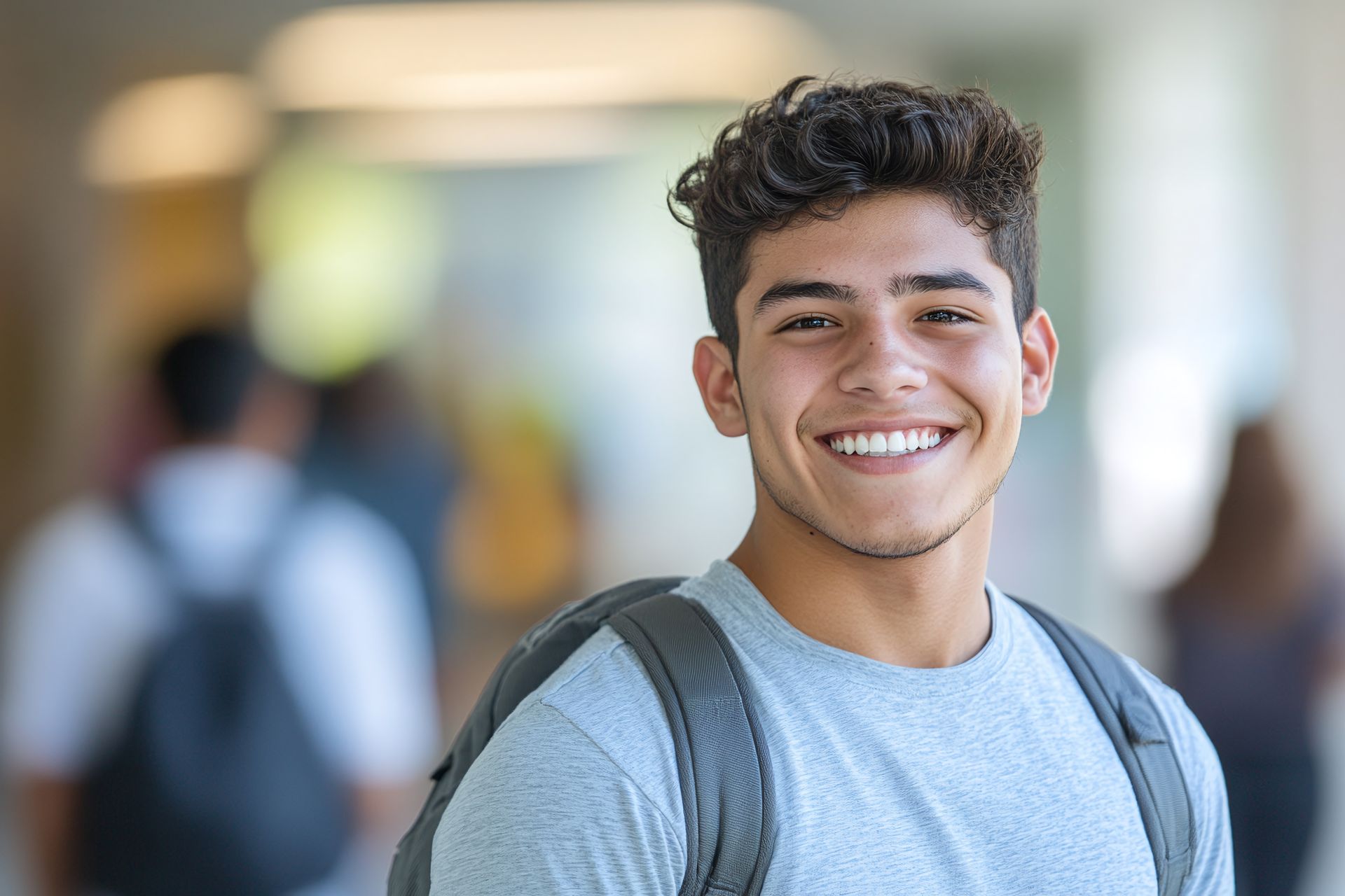 Smiling young man with curly hair and a backpack in a hallway.