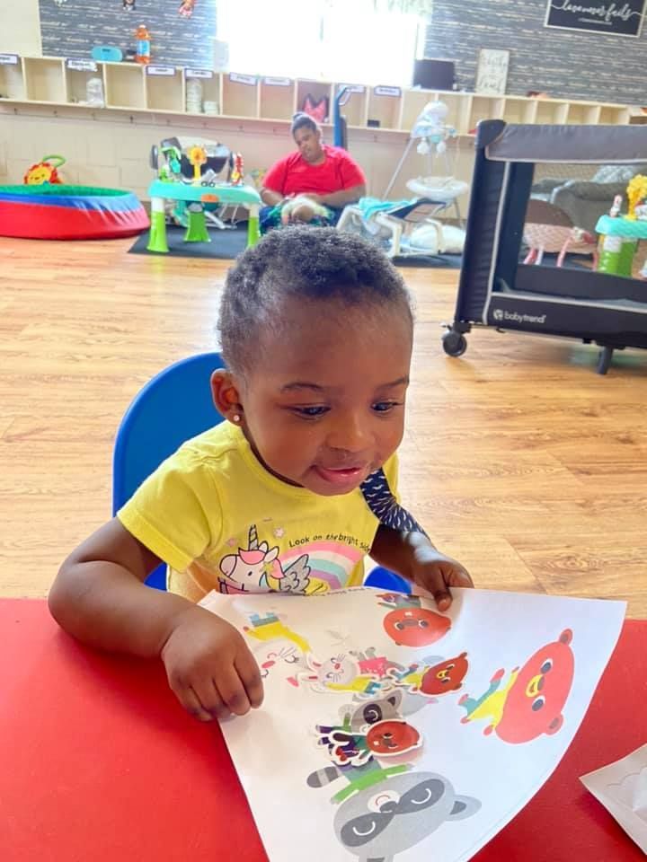 A little girl is sitting at a table looking at a piece of paper.