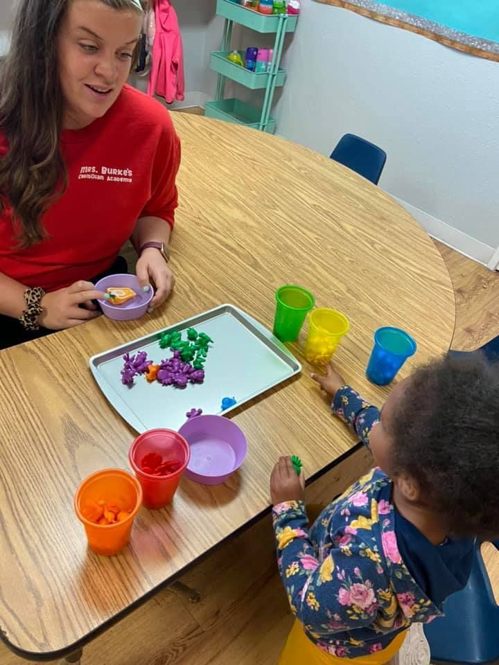 A woman is sitting at a table with a child playing with toys.