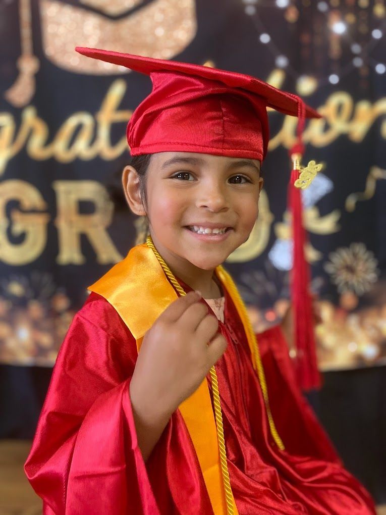 A young boy is wearing a red graduation cap and gown.