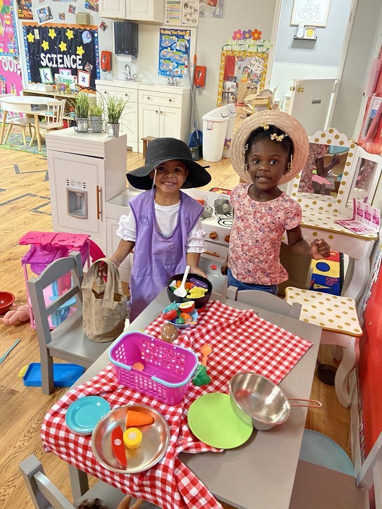 Two young girls are standing next to a table in a play room.