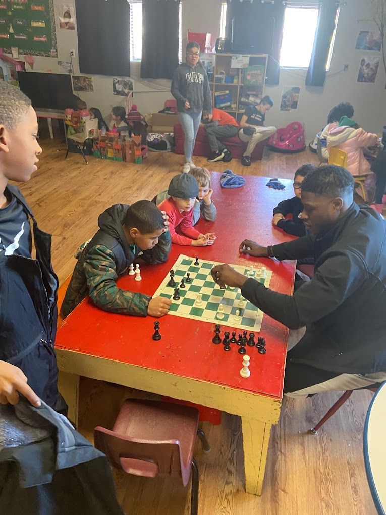 A group of children are playing chess at a table in a room.
