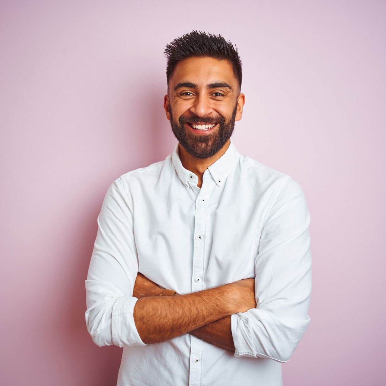 A man with a beard is standing with his arms crossed and smiling.