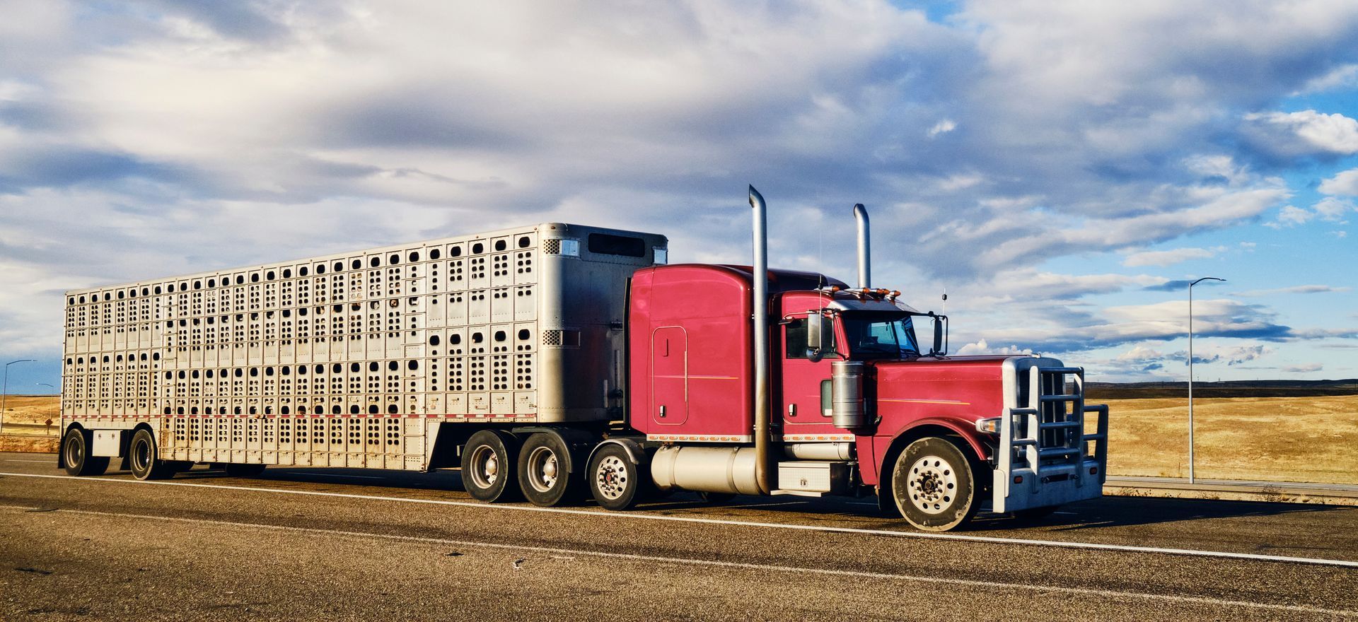 A red semi truck is driving down a dirt road.