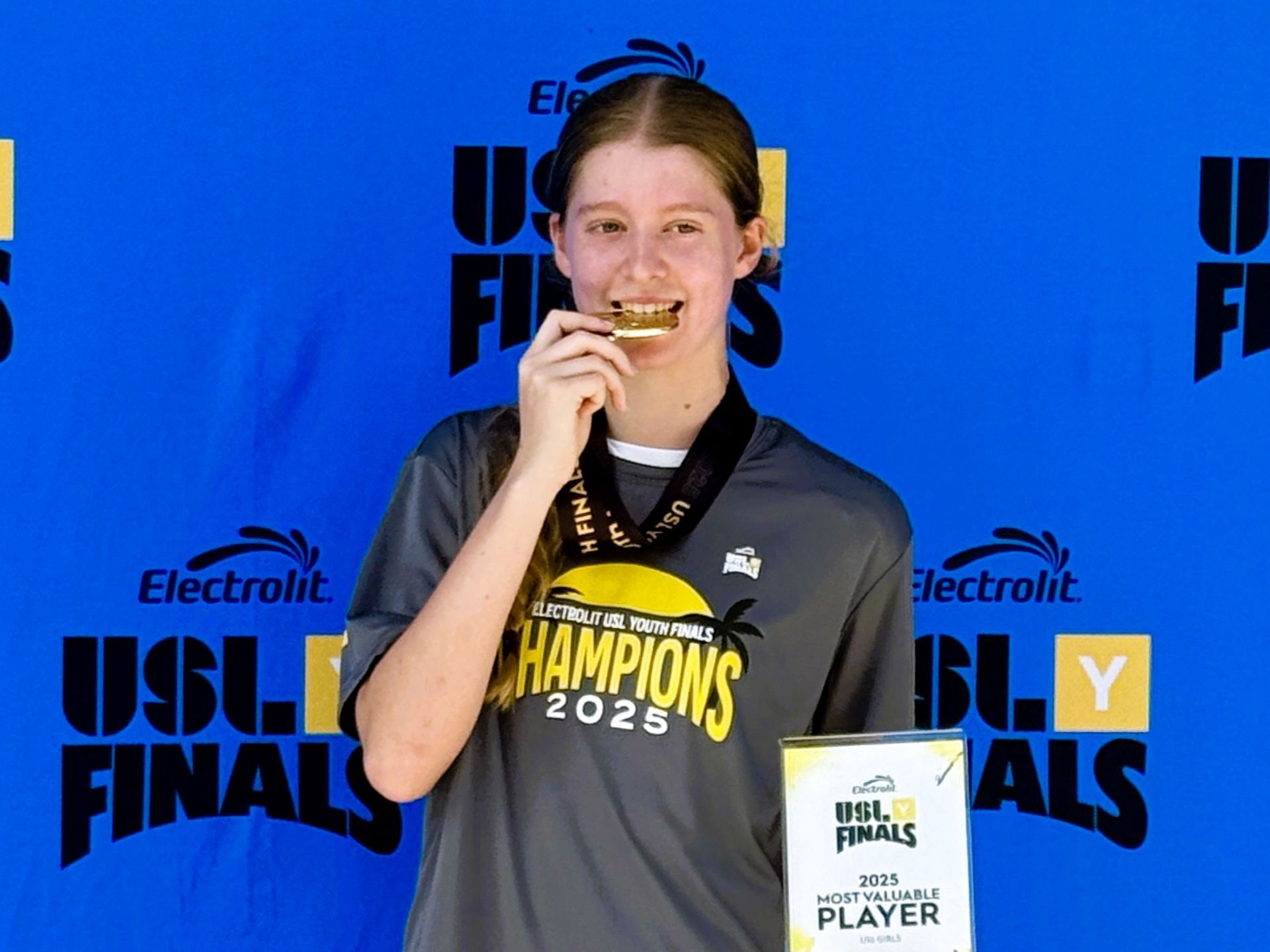 A young girl biting a soccer medal for Great Falls Reston Soccer Club Super Y USL Y program