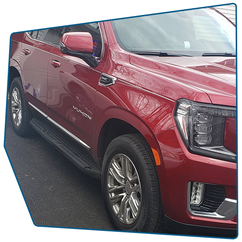 Red GMC Yukon SUV parked on asphalt. Shiny chrome wheels and black running boards are visible.