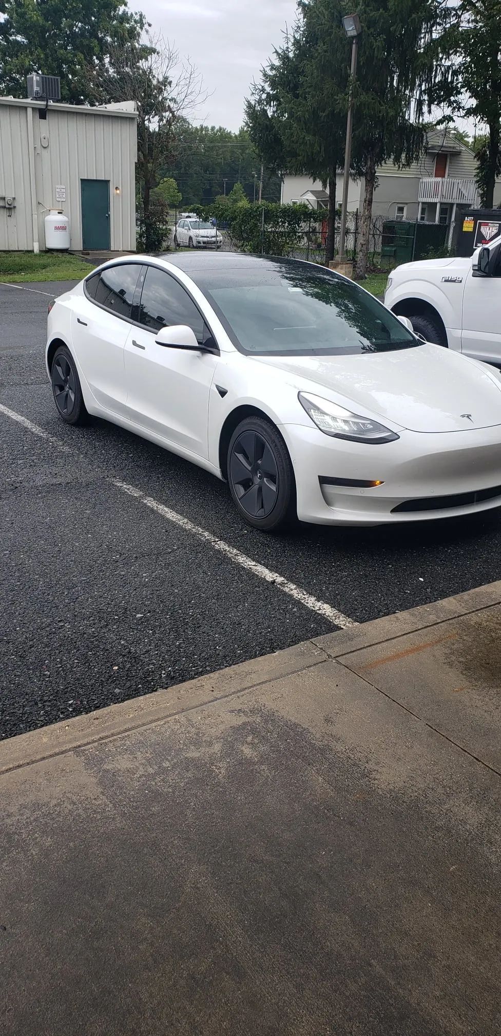 White Tesla Model 3 parked on a gravel lot near a building.