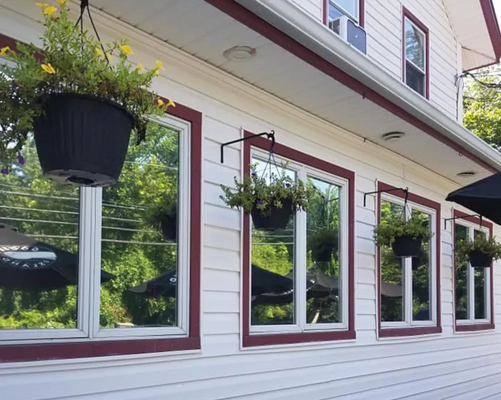 White building with red trim, windows reflect trees, hanging flower baskets.