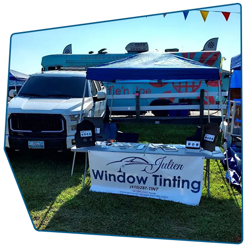 A window tinting booth at an outdoor event. White truck and blue awning with a banner that reads Julien Window Tinting. A window tinting booth at an outdoor event. White truck and blue awning with a banner that reads Julien Window Tinting.