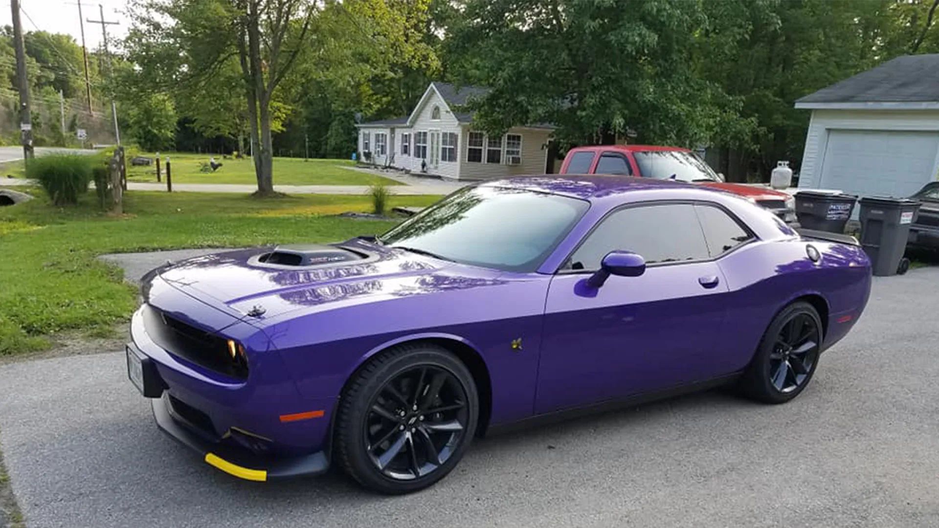 Purple Dodge Challenger parked on a driveway with a house and garage in the background.