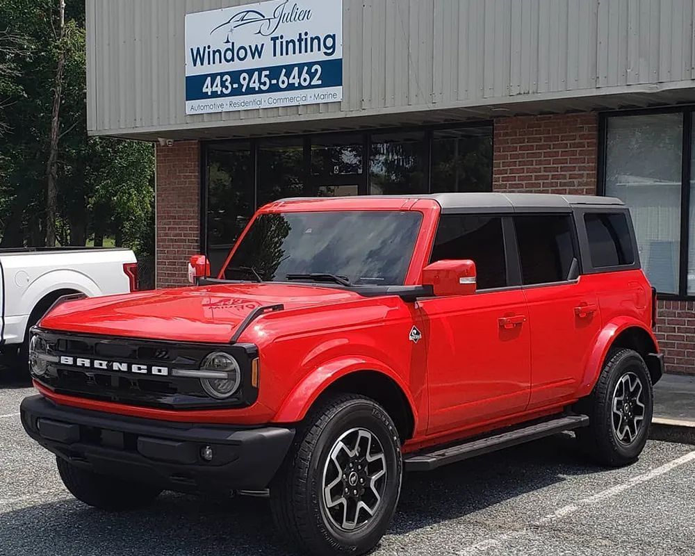 Red Ford Bronco parked in front of a window tinting business with black tinted windows.