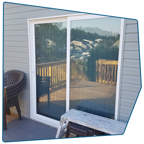 Sliding glass door on a deck, reflecting trees and buildings; chairs and a step stool are nearby. Sliding glass door on a deck, reflecting trees and buildings; chairs and a step stool are nearby.