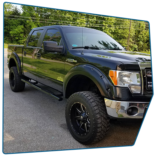 Black lifted Ford F-150 truck with black wheels and fender flares, parked on an asphalt road.