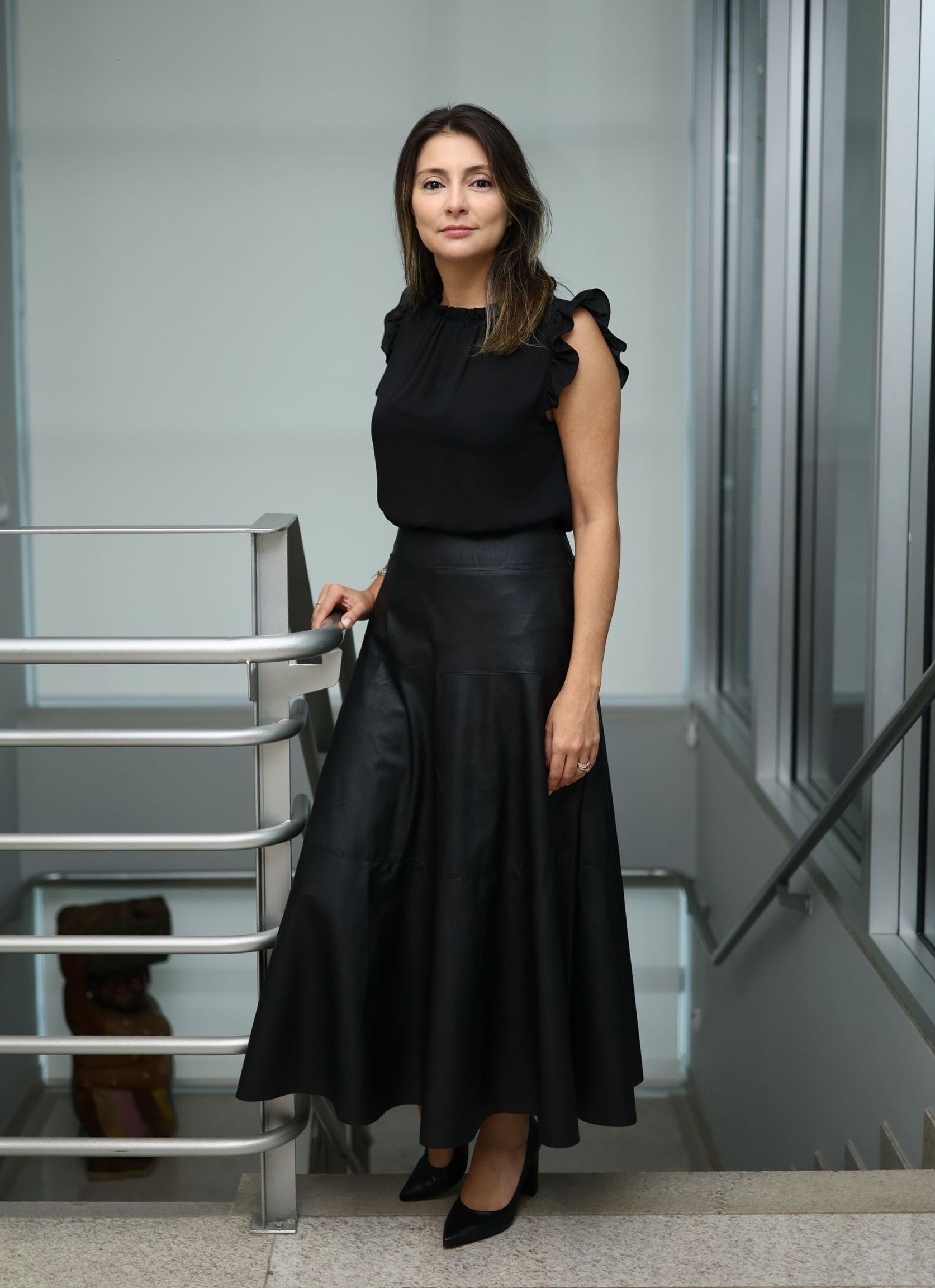 Uma mulher está parada em um lance de escadas vestindo uma saia preta e uma blusa preta.