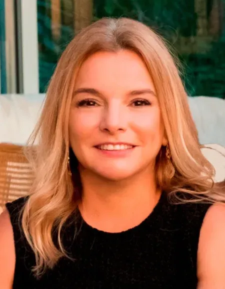 Uma mulher de cabelos loiros está vestindo uma regata preta e sorrindo.