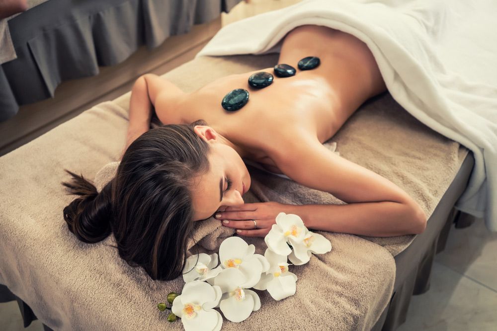 High Angle View Of Young Woman Lying Down On Massage Bed With Traditional Hot Stones Along The Spine — Hot Stone Massages in Glenfield Park, NSW