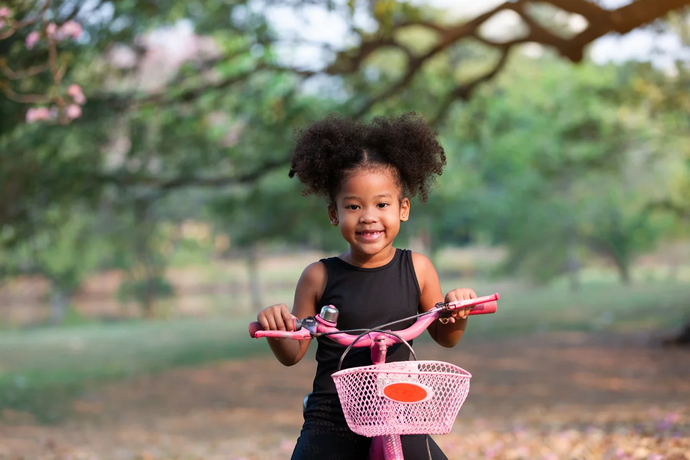 A little girl is riding a pink bicycle in a park.