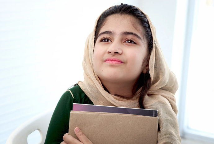 A young girl wearing a head scarf is holding a stack of books.