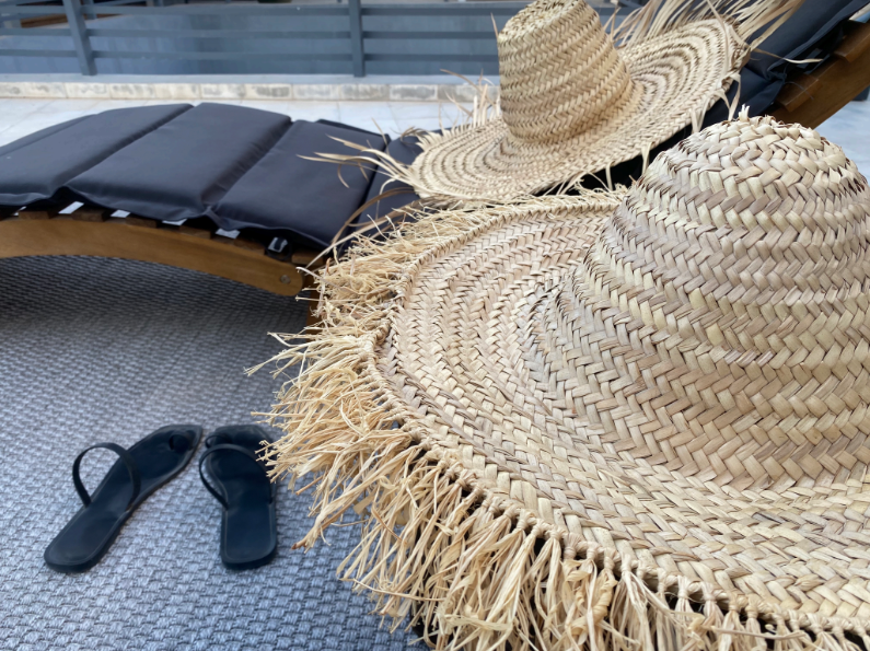 A pair of flip flops and a straw hat are sitting next to a chair.