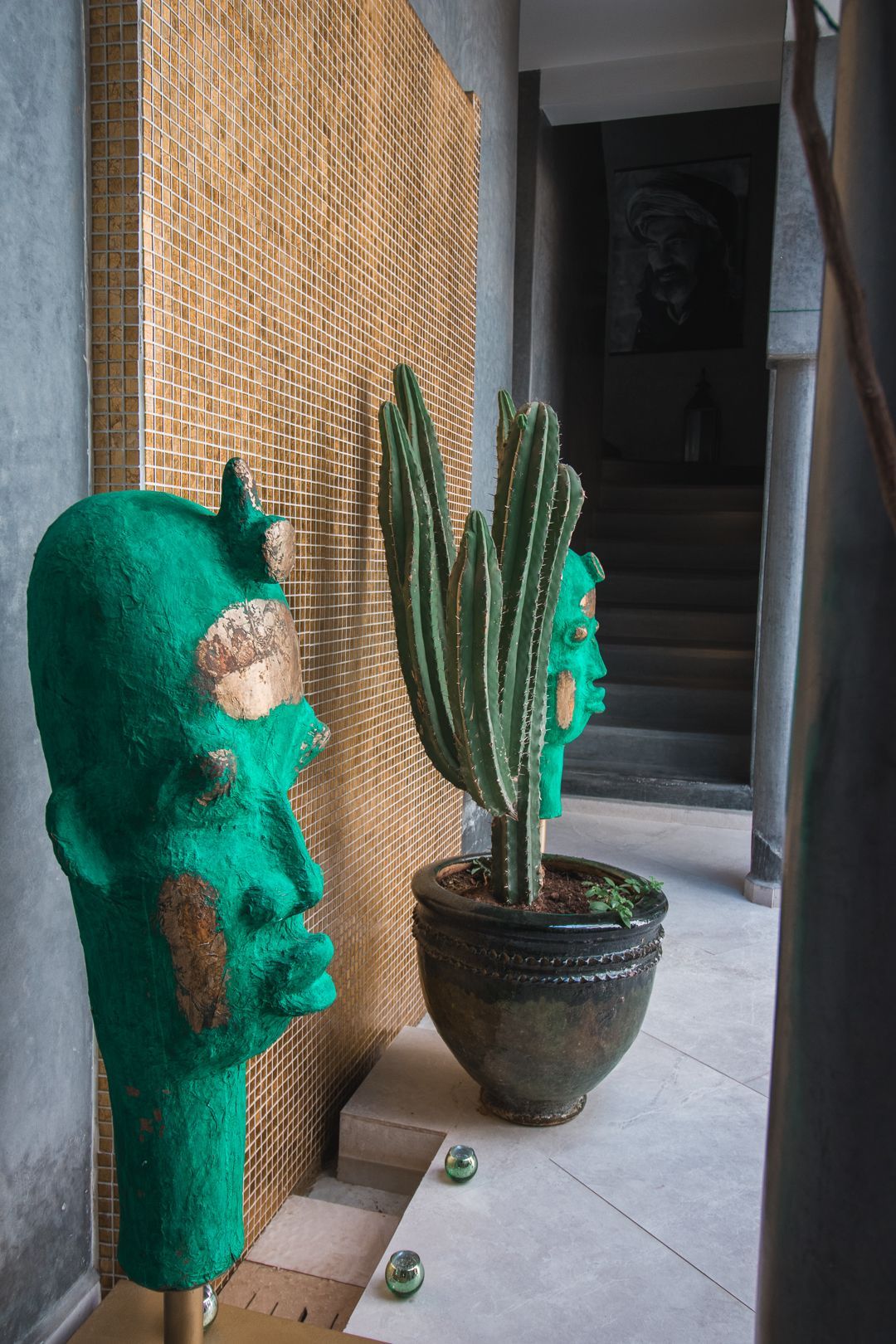 A cactus in a pot next to a green statue of a face.