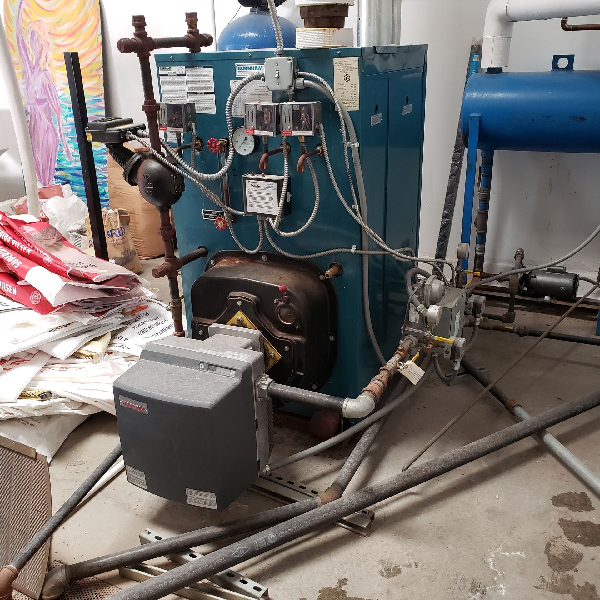 A blue industrial boiler with attached pipes and control panels in a utility room.
